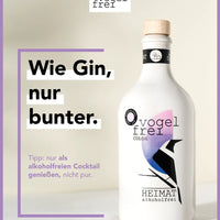 Alkoholfreier Heimat Gin „Vogelfrei Color“ mit farbiger Flasche, ideal für Essen und Trinken, auf einem Tisch präsentiert.